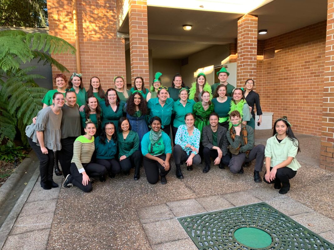 Three rows of people wearing various shades of green. They are huddled together and smiling.