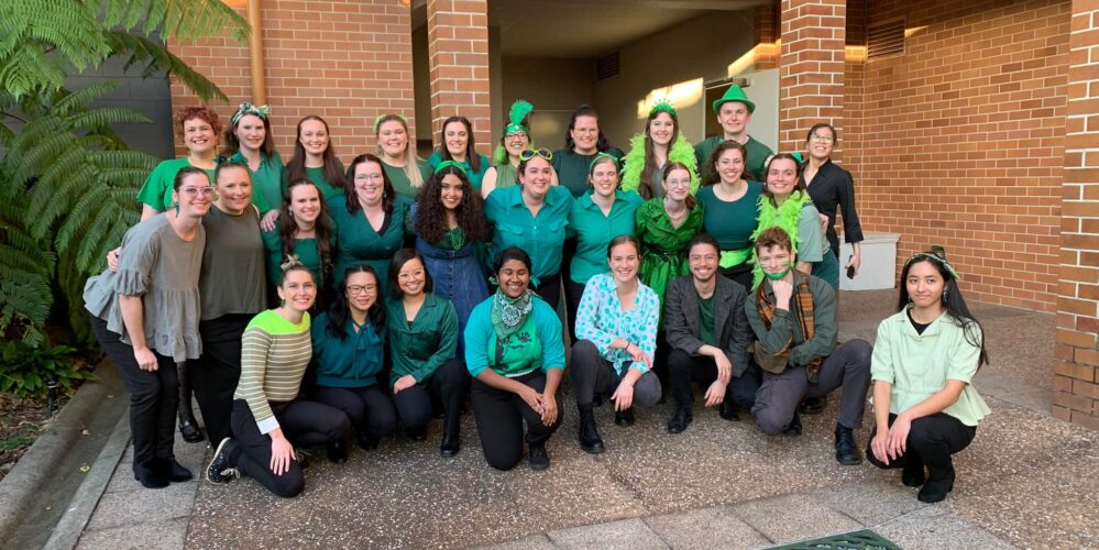 Three rows of people wearing various shades of green. They are huddled together and smiling.