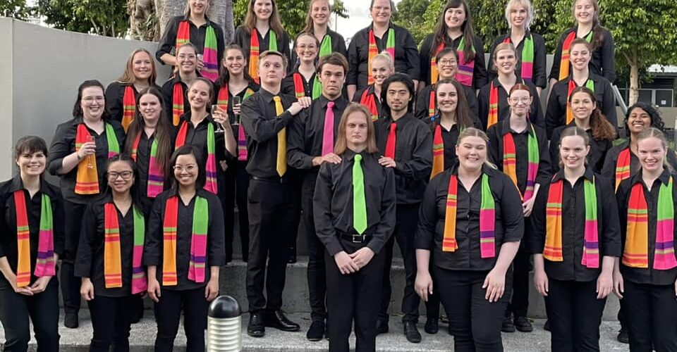 Four rows of people wearing colourful scarves standing on concrete stairs and smiling.