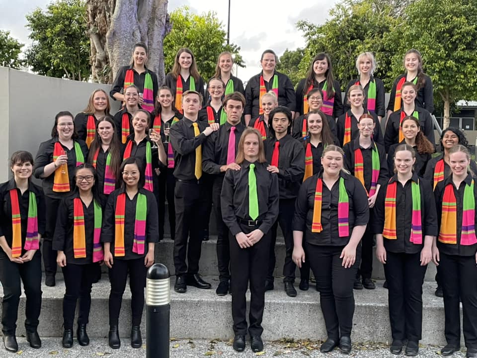 Four rows of people wearing colourful scarves standing on concrete stairs and smiling.